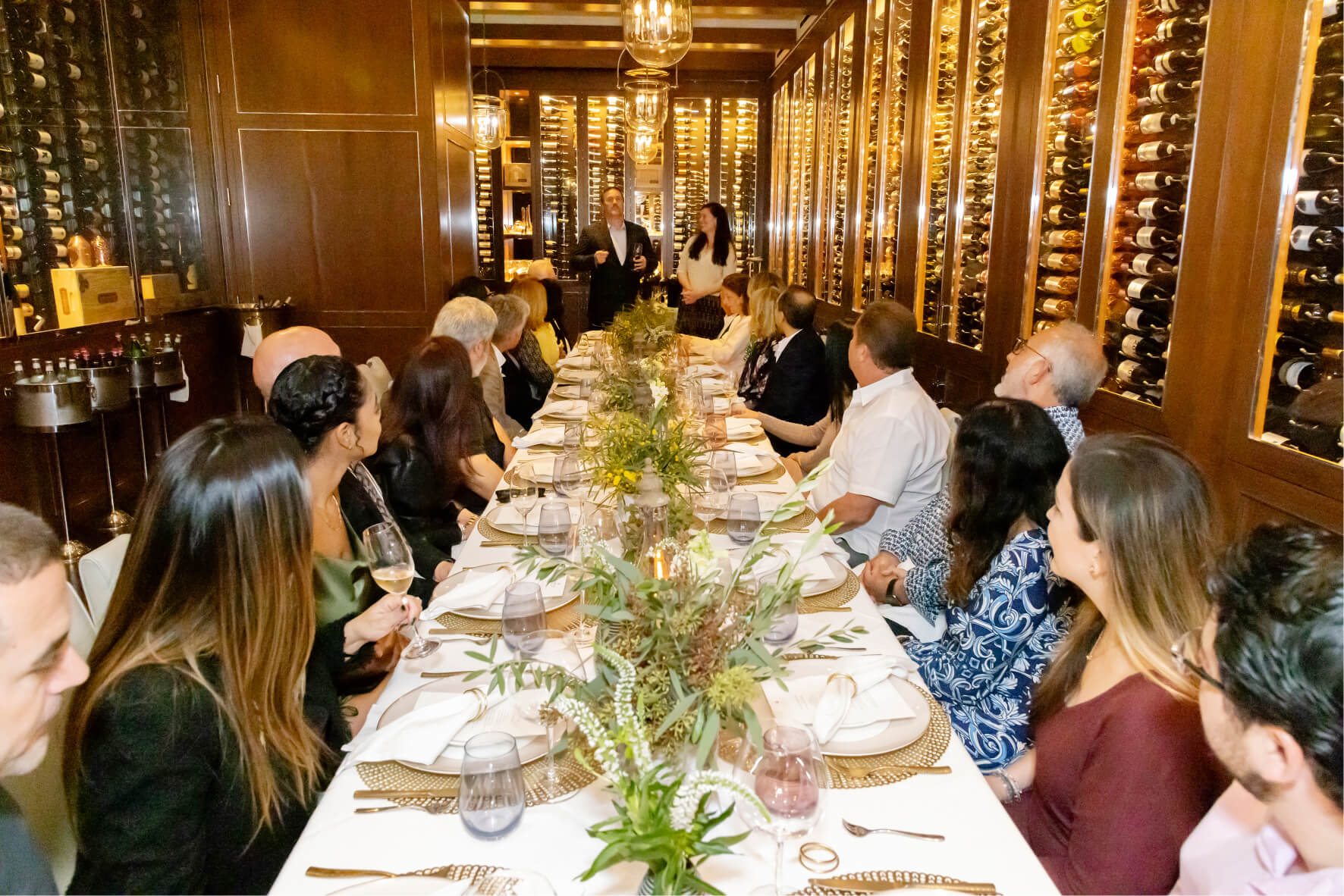 Many people sitting on a long table looking at person at the end