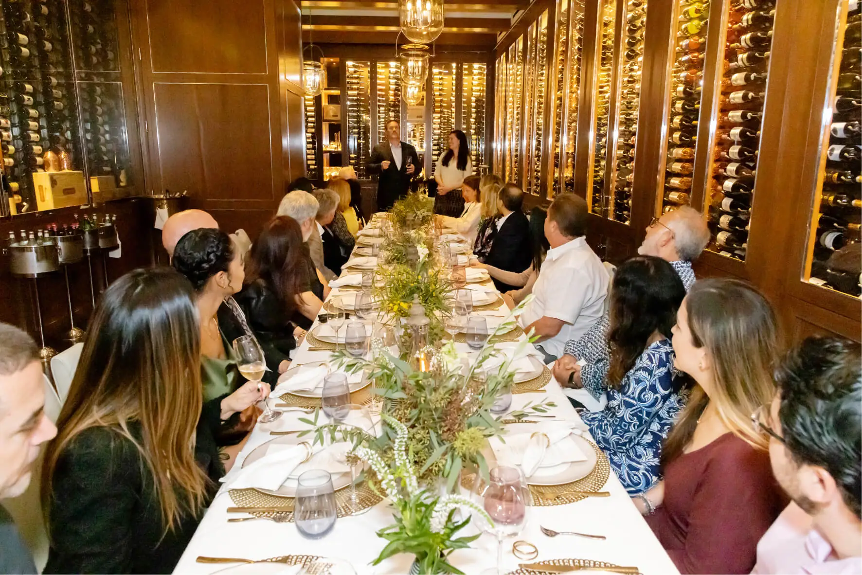 Many people sitting on a long table looking at person at the end